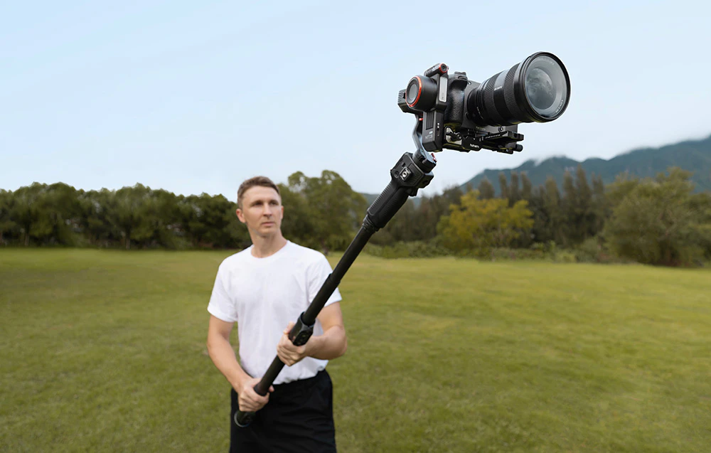 Băiat ținând un gimbal extins cu cameră atașată în aer liber