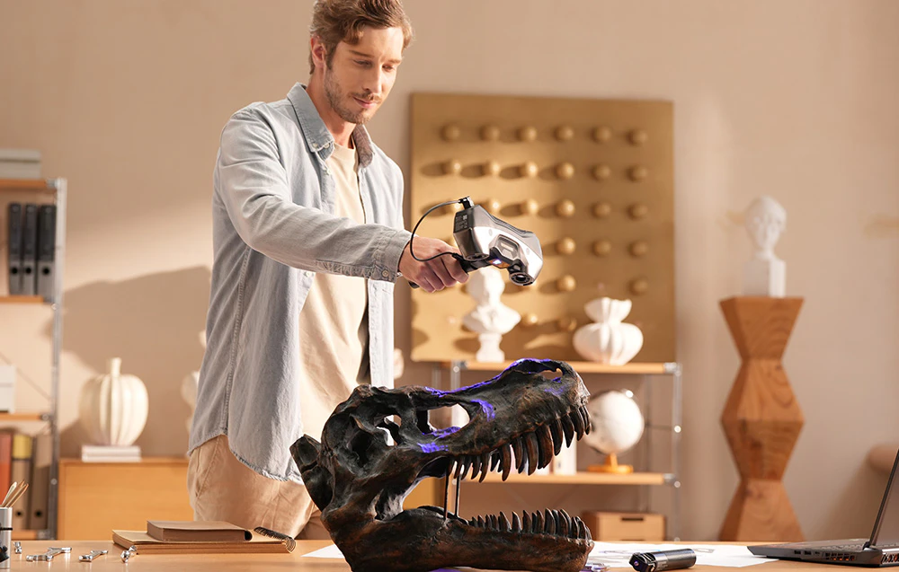 Un bărbat scanează o replică mare a unui craniu de dinozaur într-un interior luminos cu un scaner 3D