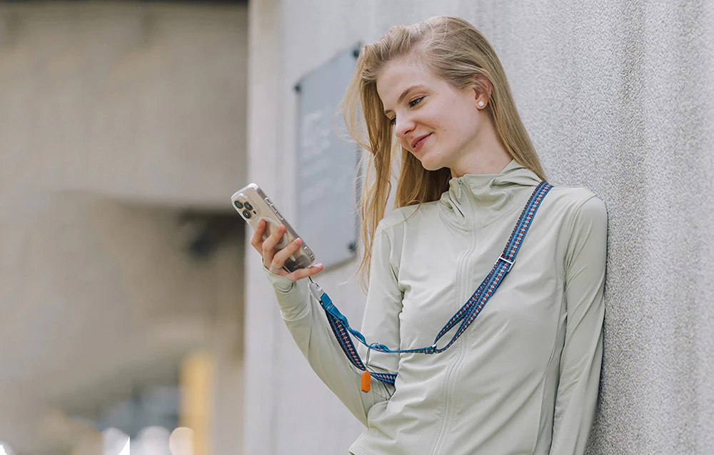 O femeie sprijinită de un perete și folosind smartphone-ul său, care este montat pe o curea de gât