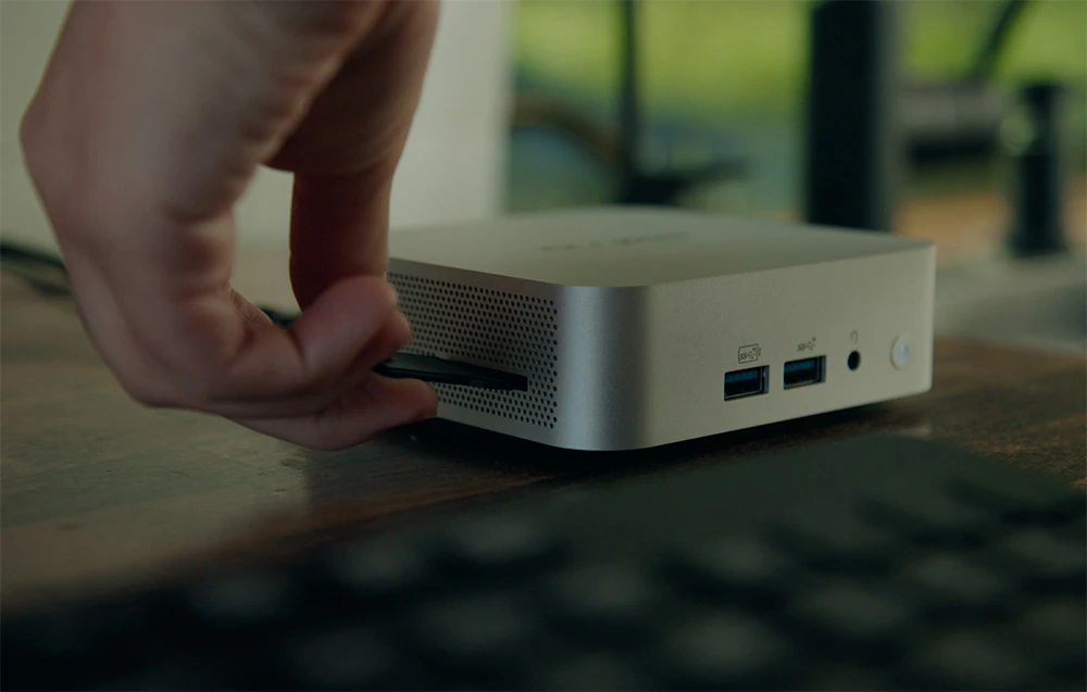 O mână introducând un card într-un mini computer Geekom