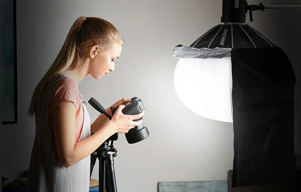 Un fotograf care examinează fotografiile pe un aparat foto montat pe un trepied, iluminat de lumina moale provenită de la o softbox Neewer.