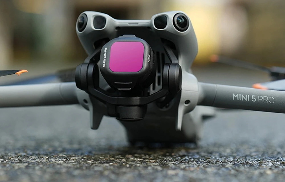 Drona DJI Mini 5 Pro cu filtrul roz instalat pe camera foto, vedere din față pe sol