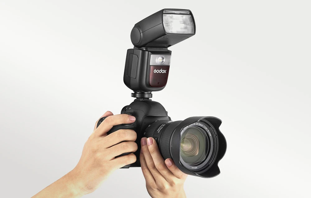 Mâini ținând un DSLR cu un bliț Godox V860III montat și un obiectiv