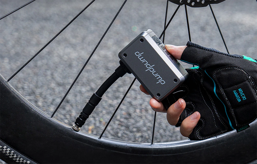 O imagine a unei pompe de bicicletă compacte ținută într-o mână pe un fundal verde estompat de copaci.