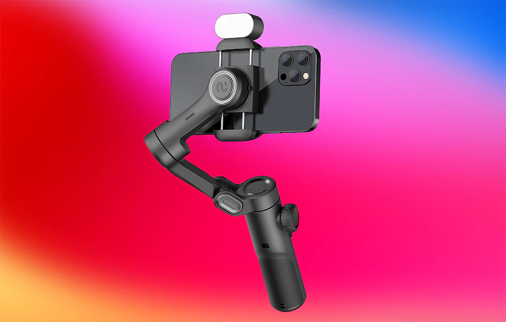 Prim-plan al părții din spate a unui smartphone montat într-un gimbal cu un accesoriu suplimentar în partea de sus, pe un fundal roz strălucitor.