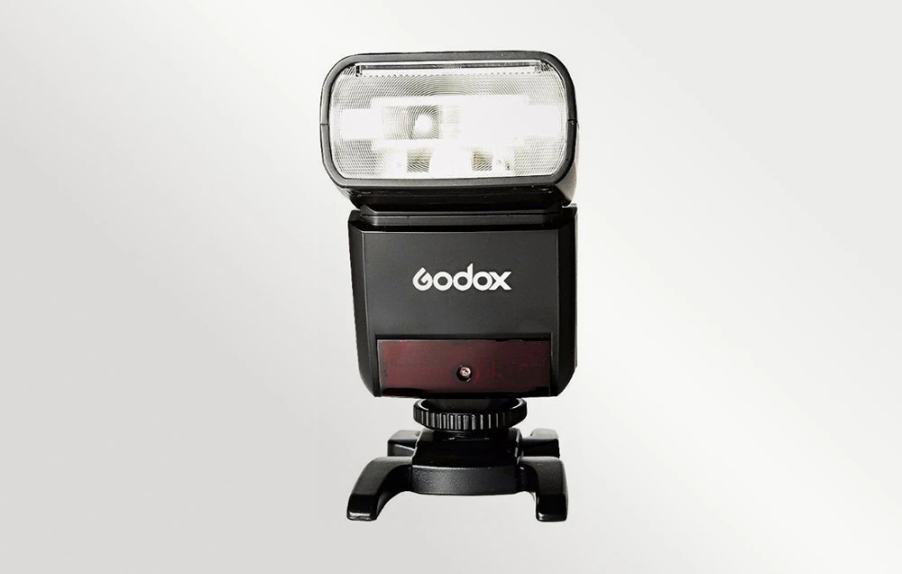 Blițul Godox TT350 negru montat pe un suport din plastic, vedere frontală pe un fundal deschis