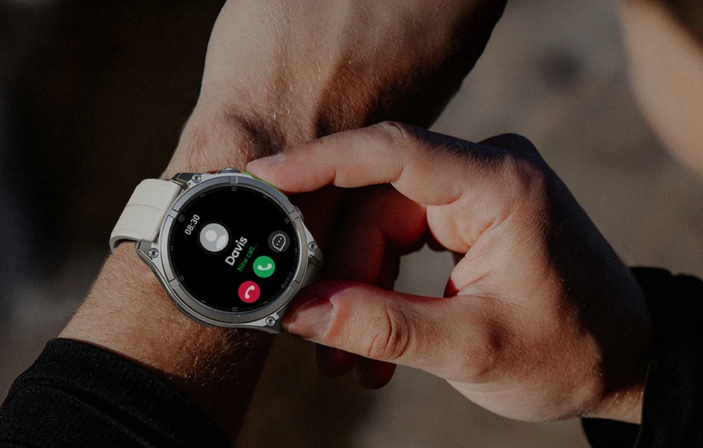 O mână care ține un smartwatch cu curea albă, ecranul pentru apeluri primite fiind vizibil pe cadran
