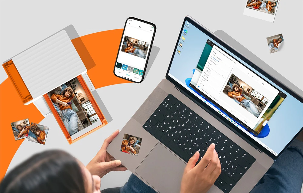 O femeie care folosește un laptop cu o fotografie deschisă pe ecran, care a fost imprimată pe imprimanta portabilă aflată lângă ea