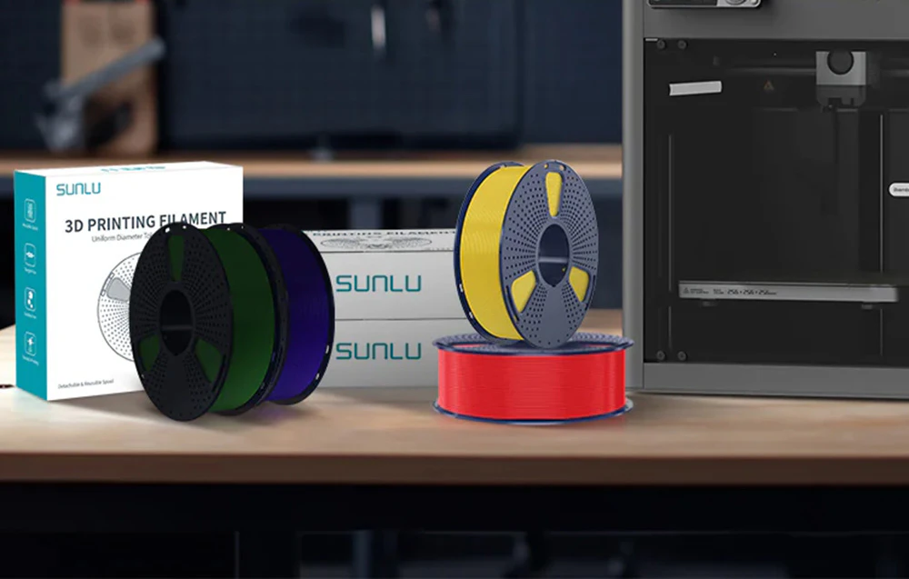 Bobine de filament de imprimare Sunlu și cutii așezate pe o bancă de lucru lângă o imprimantă 3D.