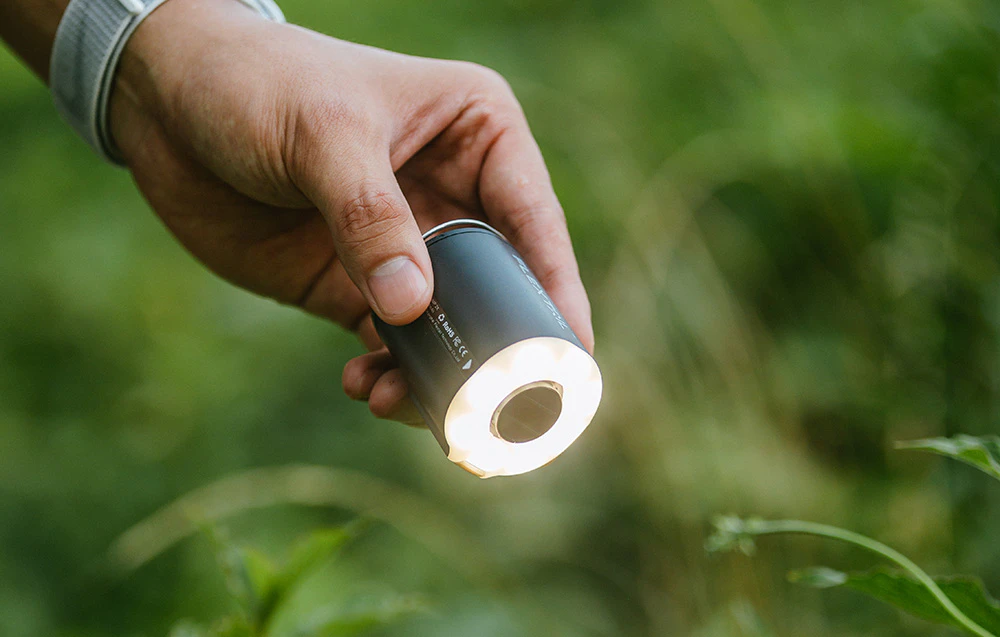 O mână care ține pompa Flextail cu panoul de lumină LED activat, folosind-o ca lanternă de camping pe un fundal verde