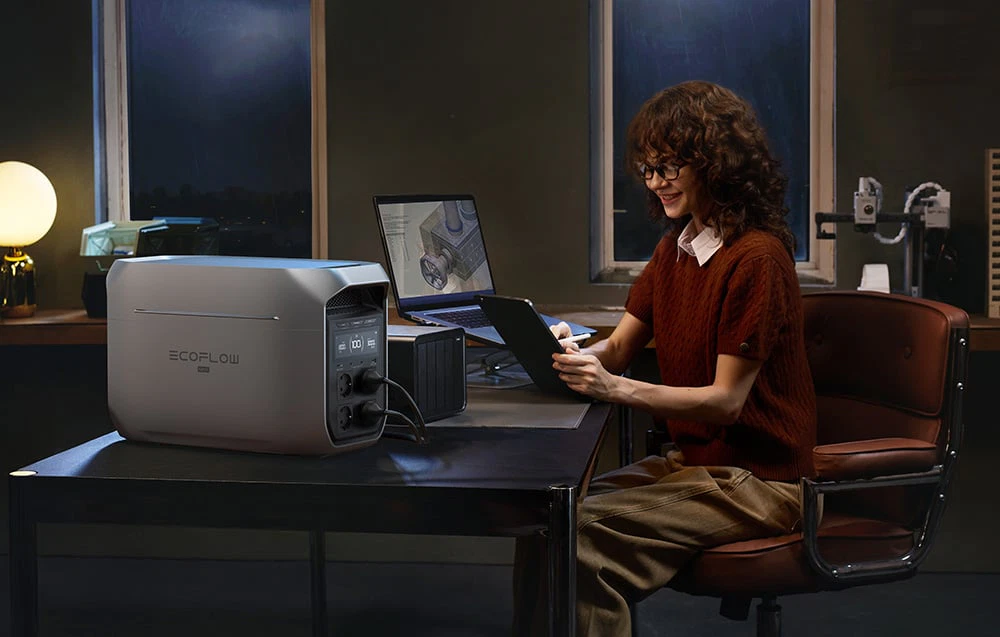 O femeie lucrează seara la birou cu un laptop alimentat de o stație EcoFlow Delta 3 Max.