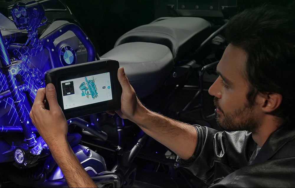 Un bărbat îmbrăcat într-o jachetă de piele ține un scaner 3D îndreptat spre motorul unei motociclete BMW