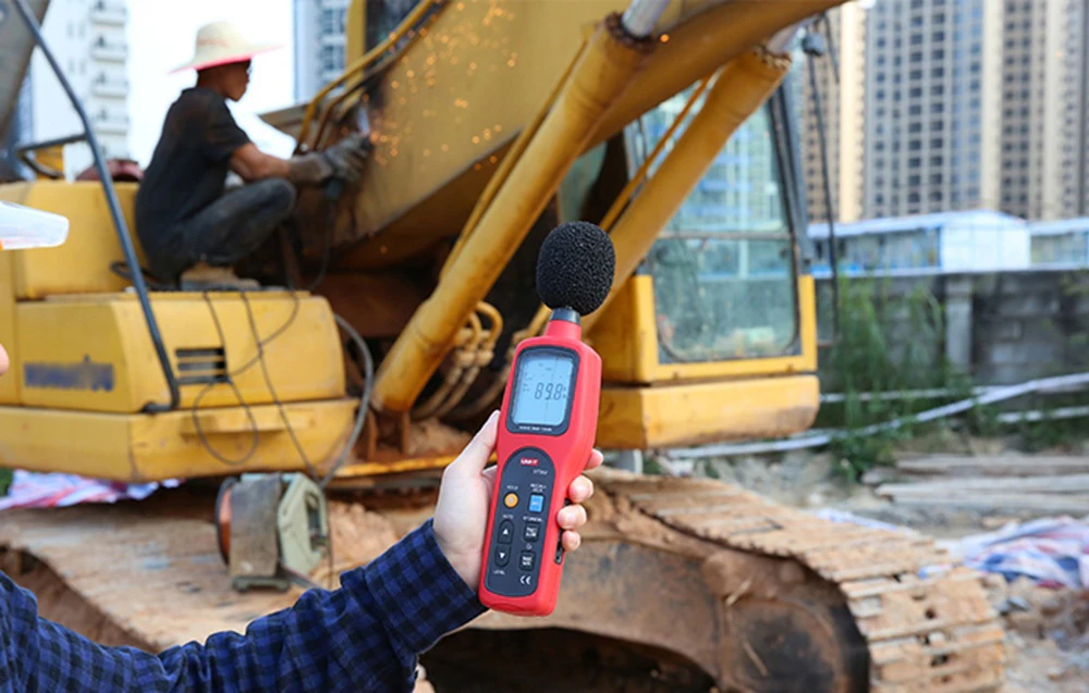 Sonometru portabil Uni-T pe un șantier de construcții, cu un excavator în fundal