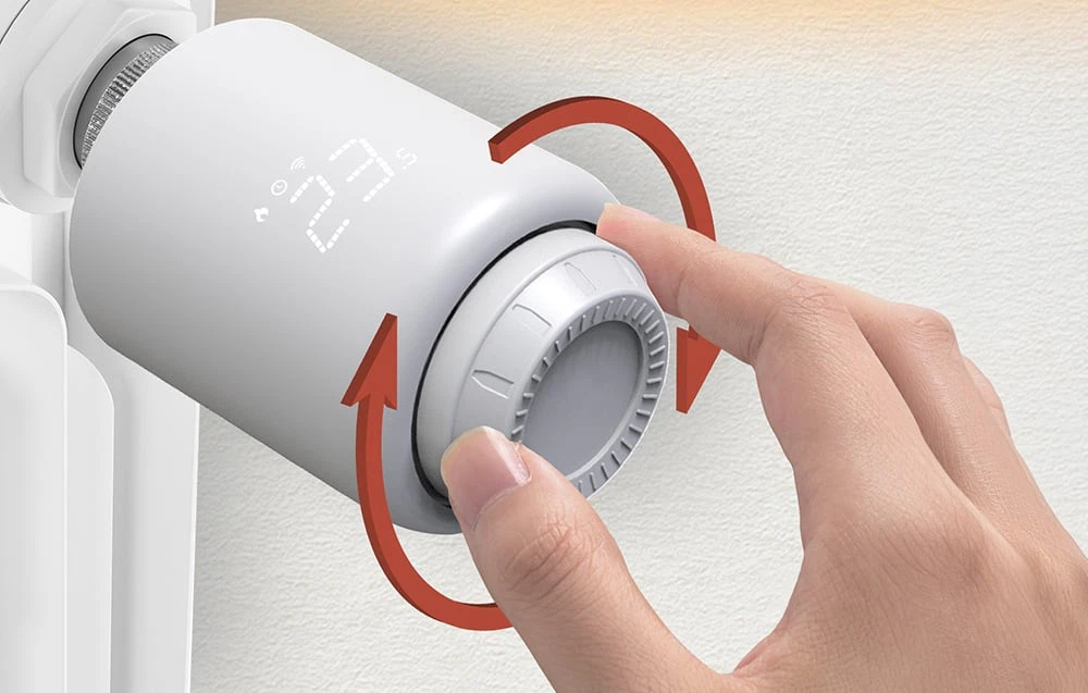 O persoană care rotește butonul unui cap termostatic inteligent montat pe un radiator.