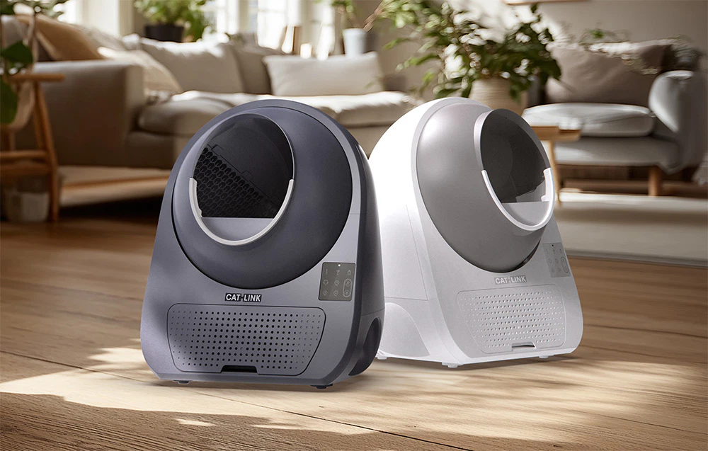 Două cutii automate de nisip CatLink, una gri și una albă, așezate una lângă alta într-un living luminos