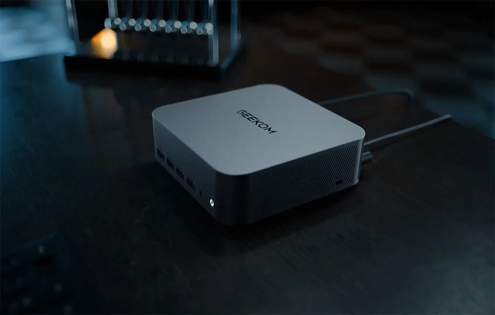 Un MINI PC Geekom gri cu un cablu conectat pe un birou negru