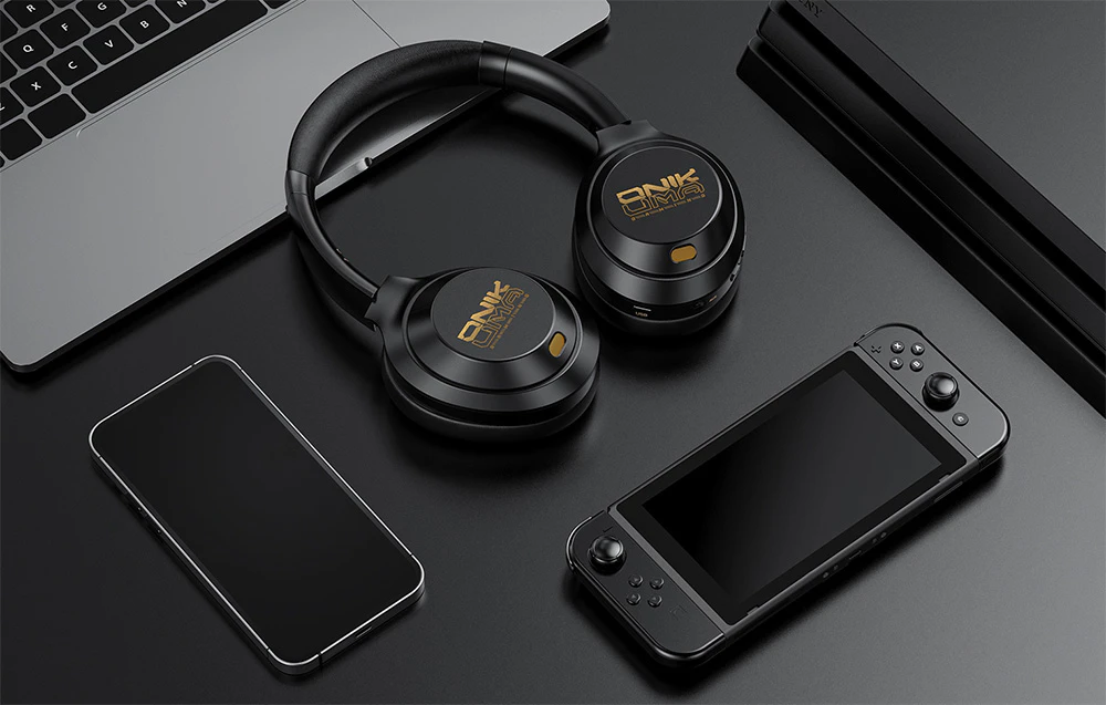 Căști in-ear negre așezate pe un laptop lângă un smartphone și o consolă mobilă