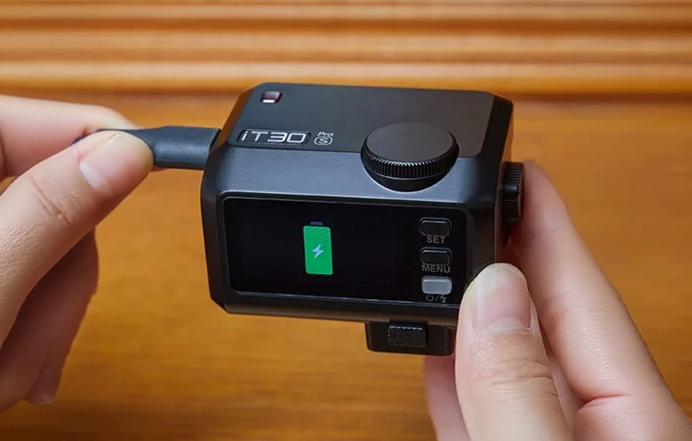 Un blitz Godox iT30 Pro negru ținut în mână în timp ce se încarcă prin intermediul unui cablu USB