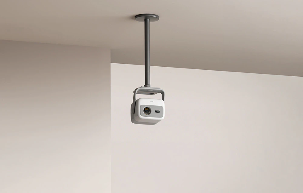 Un proiector pe un suport de tavan îndreptat către un perete de culoare deschisă într-un interior modern.