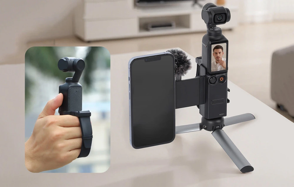 Aparat foto cu suport pentru smartphone și microfon plasat pe masă, prim plan al mâinii care ține dispozitivul