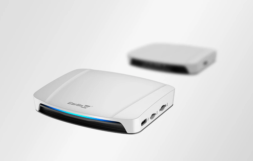 2 adaptoare wireless pentru mașină. În fundal, interiorul unei mașini și un ecran pe care sunt redate videoclipuri.