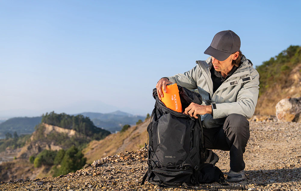Un bărbat pune o saltea Flextail pliată în rucsacul său în munți.