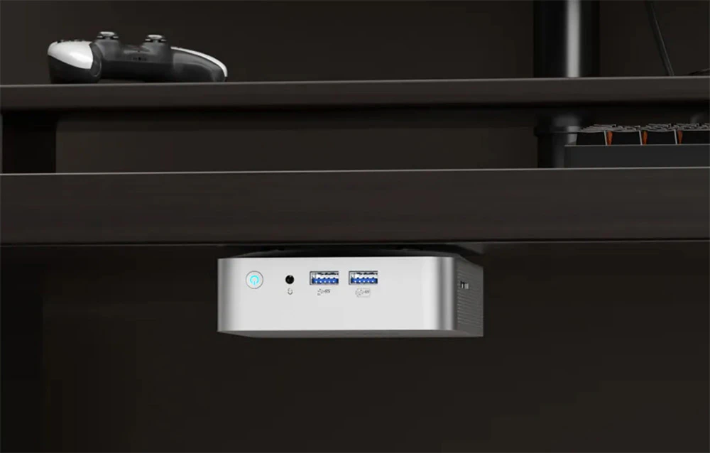 Un mini PC montat sub blatul unui birou. Este vizibil panoul frontal cu butonul de pornire și porturile.