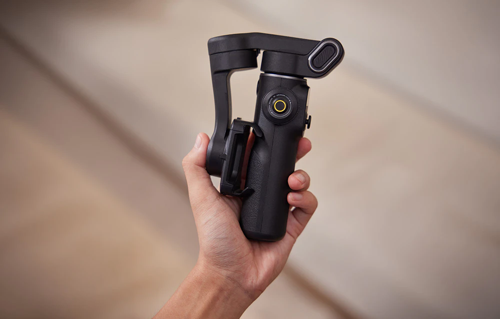 O mână care ține un gimbal negru pliat, într-o formă compactă.